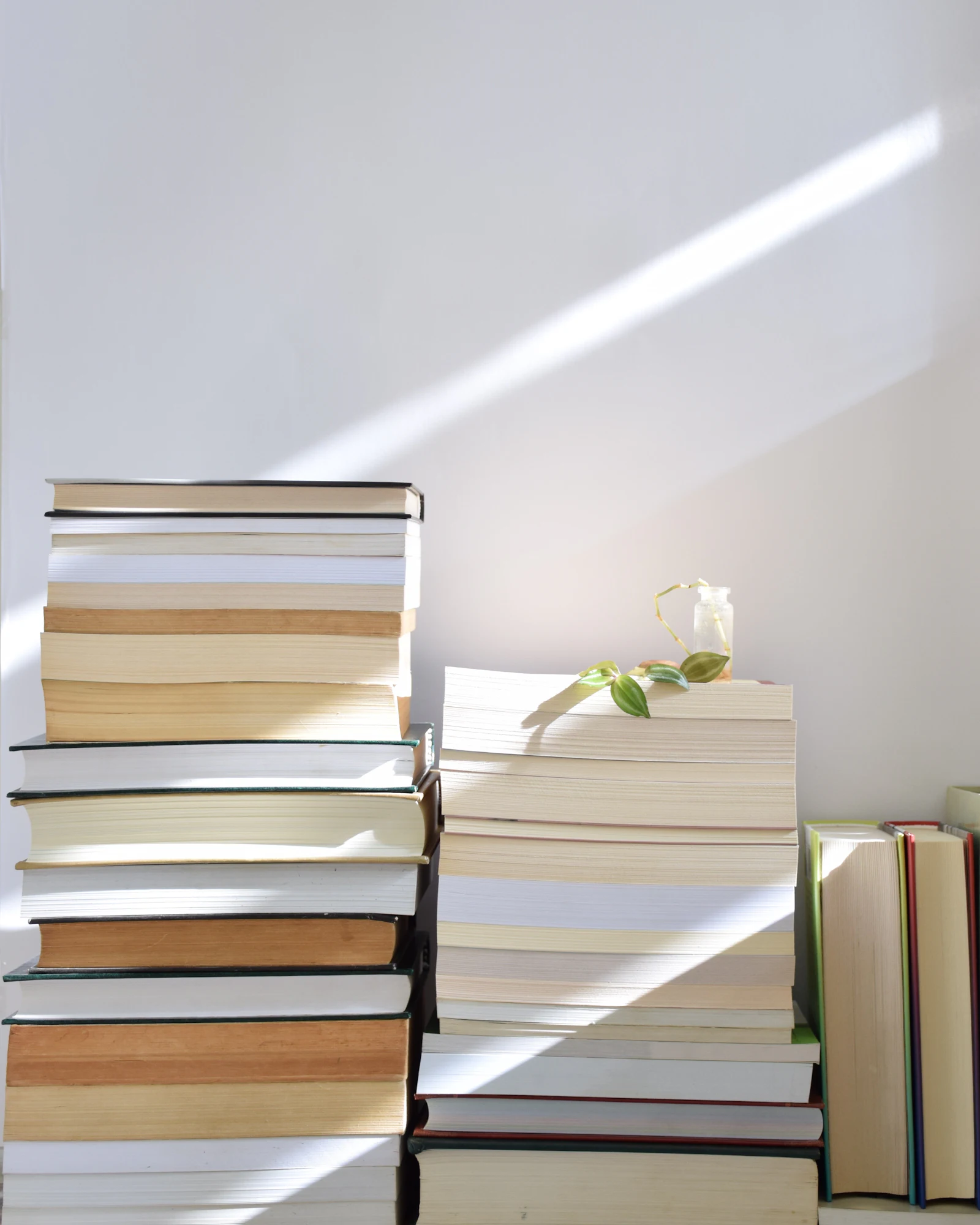 Stapels boeken tegen een witte muur, met een streep zonlicht erboven